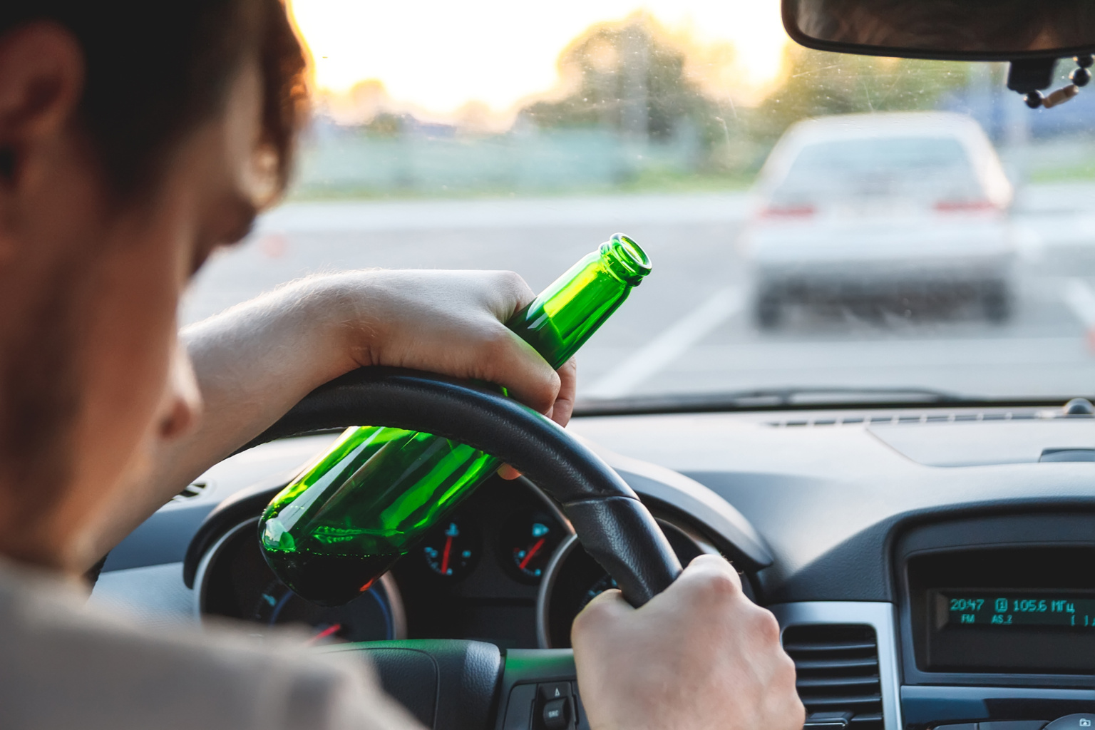 A Man Driving A Car With A Bottle Of Beer